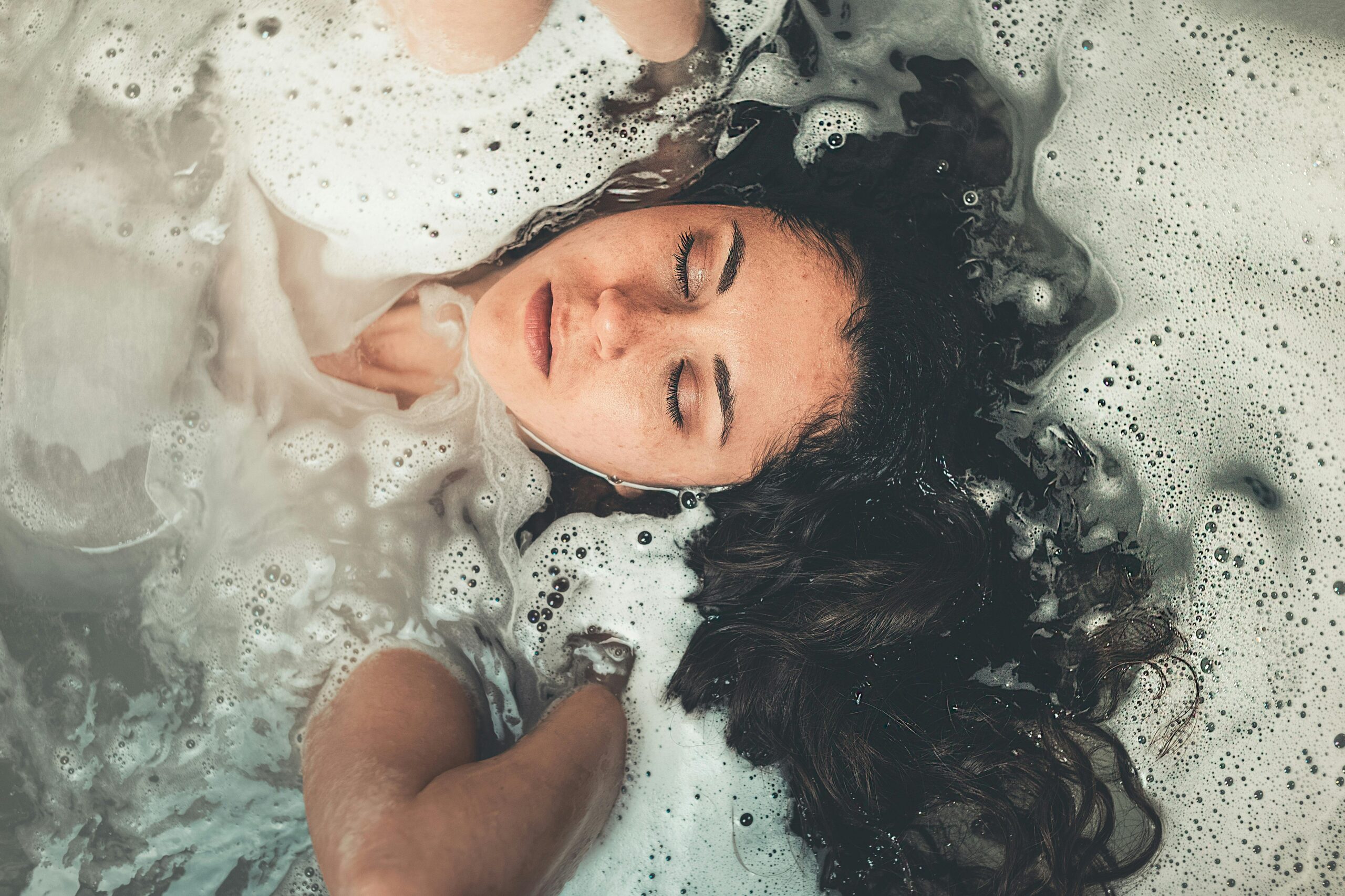 Young woman submerged in a relaxing bubble bath, eyes closed in tranquility.